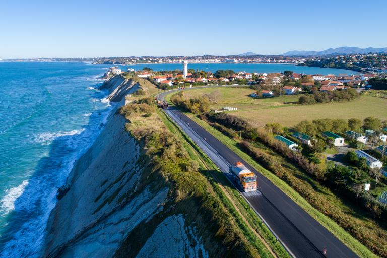 Pose d’un revêtement routier drainant sur voie côtière sinueuse avec engins de chantier, préparation de plateforme et protections des berges.