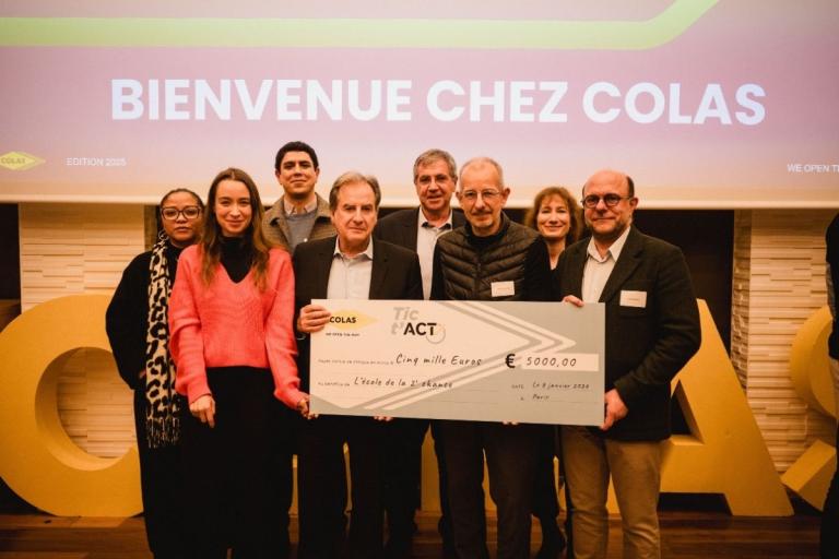 Remise de chèque Tic & Act chez Colas : groupe sur scène tenant un grand chèque symbolique devant l’écran « Bienvenue chez Colas ».