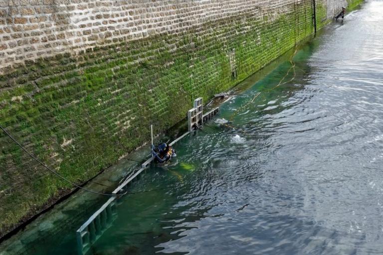 Trancheuse et pelleteuse en train d’élargir une fouille en campagne pendant la pose d’une canalisation bleue, avec blindage en place et ouvriers en EPI ; matériel et déblais positionnés le long de la tranchée.