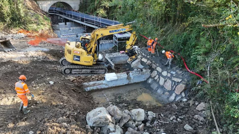 Chantier de rivière en cours avec un engin de type pelle jaune et des collaborateurs Colas