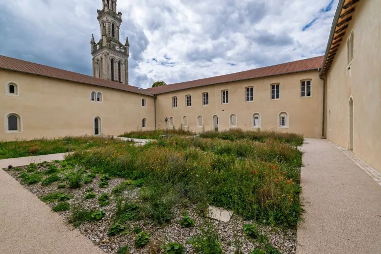 Cours intérieur avec de l'urbalith et des batiments : Cour intérieure d'un bâtiment historique rénové, aménagement paysager en prairie sèche au centre, cheminements piétons périphériques et bâti aux façades enduites en bon état apparent.