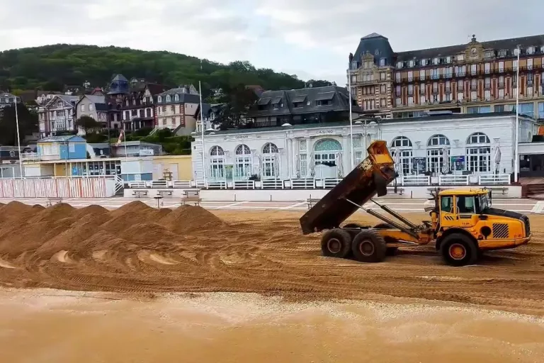 Tombereau déversant du sable sur la plage de Houlgate devant le front de mer et le casino dans le cadre des travaux de rééquilibrage.