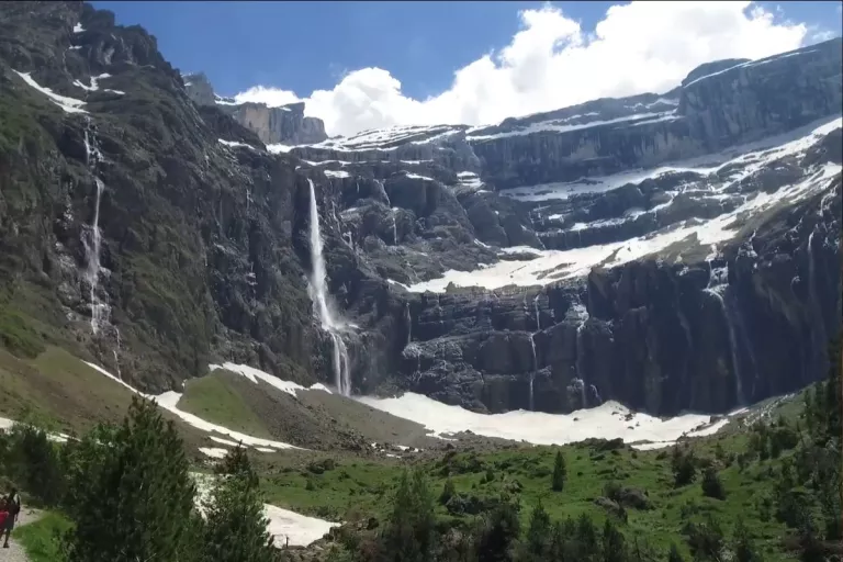 Cirque montagneux enneigé traversé par plusieurs cascades au-dessus d’une vallée verdoyante.
