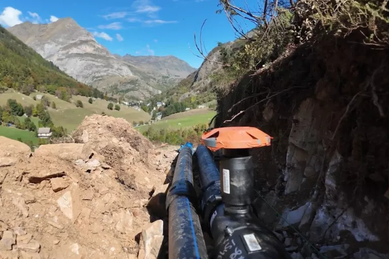 Canalisations installées dans une tranchée avec un paysage de montagne en arrière-plan.
