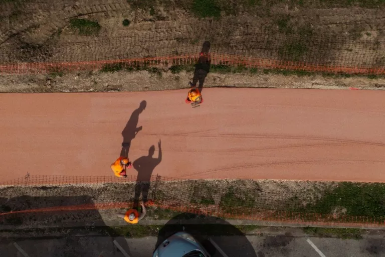 Vue aérienne de trois ouvriers intervenant sur le revêtement d’une piste cyclable.