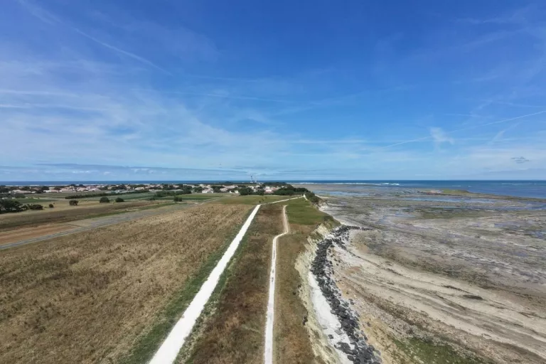 Vue aérienne d’un cheminement clair longeant des espaces naturels et le littoral à marée basse.