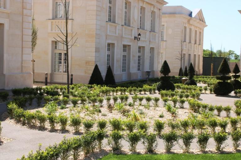 Parterres de buis, arbustes taillés et jeunes arbres devant les façades classiques des bâtiments du Puy du Fou.