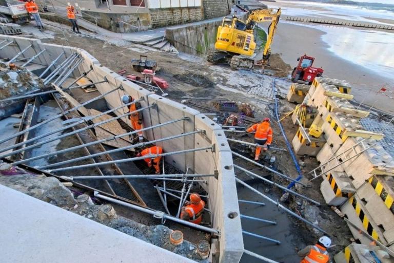 Ouvriers et engins sur un chantier de soutènement en bord de mer à Saint-Malo