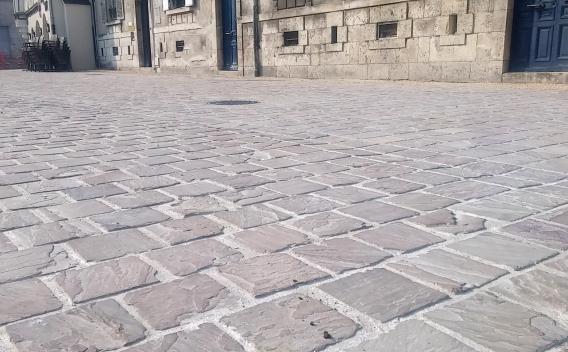 Une rue pavée en pierre claire, bordée de façades anciennes aux portes bleues et volets fermés, captée en perspective basse.
