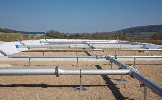 Vue d’ensemble d’un bassin filtrant en chantier, équipé d’un réseau de canalisations inox sur supports et géotextile, prêt pour la distribution et le drainage des effluents.