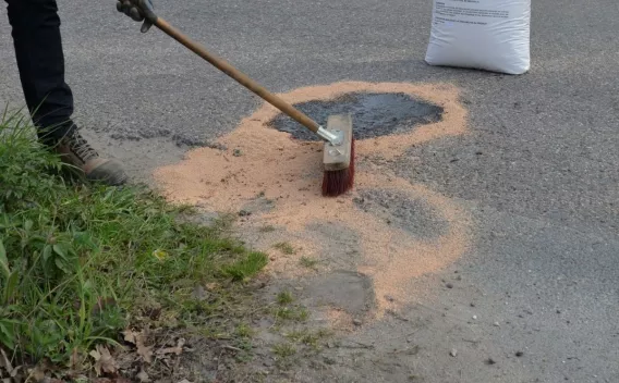 Personne balayant un absorbant en granulés sur une zone souillée d’une chaussée, sac de produit absorbant posé à proximité.