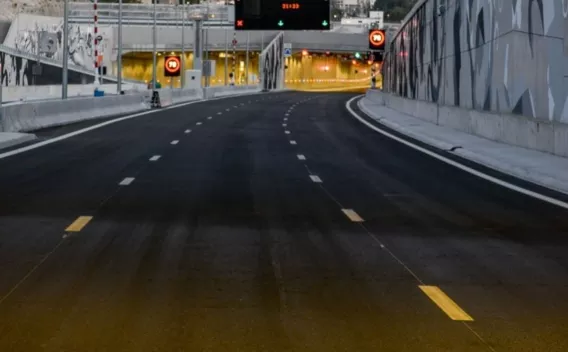 Une flèche verte guide les véhicules vers un tunnel urbain neuf, avec en arrière-plan une ville nichée au pied des collines.