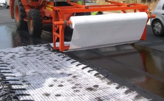 Vue rapprochée d’un engin déroulant un géotextile sur une chaussée fraîchement enduite dans le cadre d’une réfection routière.