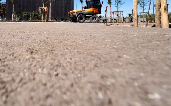 Vue aérienne d’un engin et d’une équipe réalisant une piste piéton/cyclable claire au travers d’un boisement dense, avec machine de finissage et opérateurs le long du bord.