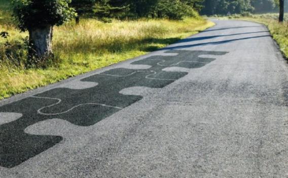 Une route paisible en campagne dont un tronçon est réparé avec un motif original en forme de pièces de puzzle.