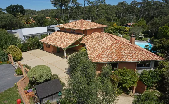 Allure méditerranéenne : une grande maison aux toits en tuiles romanes entourée d’un jardin boisé avec piscine, vue aérienne mettant en valeur l’aménagement paysager.