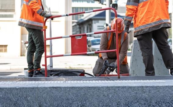 Trois ouvriers en tenue de sécurité travaillent autour d’une ouverture dans le sol, protégée par une barrière de chantier.