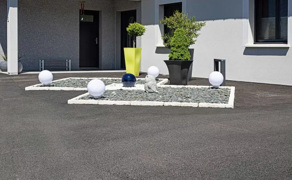 Un parterre contemporain de graviers et de sphères lumineuses encadre l’entrée élégante d’une maison moderne.