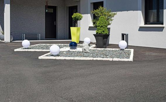 Un parterre contemporain de graviers et de sphères lumineuses encadre l’entrée élégante d’une maison moderne.