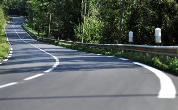 Un finisseur étale une couche d’enrobé sur une route de campagne : des ouvriers en haute visibilité surveillent la machine pendant que le matériau est déposé et prêt au compactage, encadré par des champs et un accotement herbeux.