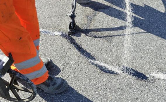 En plein soleil, un agent en orange scelle une fissure au trait blanc, prolongeant la vie de la route.