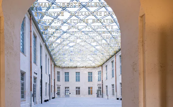 Cour intérieure restaurée d’un bâtiment patrimonial, couverte d’une verrière artistique composée de mots découpés, créant un puits de lumière au-dessus des façades en pierre claire.