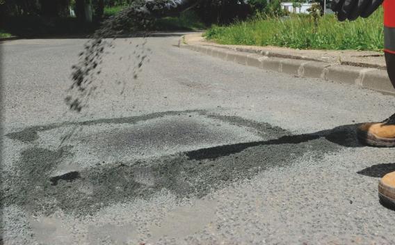 Trois emplacements colorés (jaune, rouge, noir) et un emplacement bleu réservé aux personnes handicapées, tous bordés de lignes blanches, devant une barrière et des voitures en retrait.