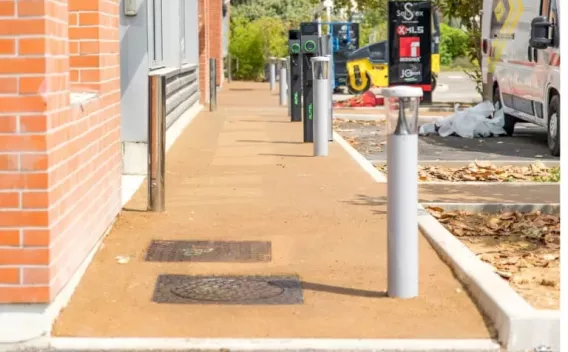 Trottoir en enrobé coloré posé dans un aménagement urbain, bordé de bornes et d'espaces végétalisés.