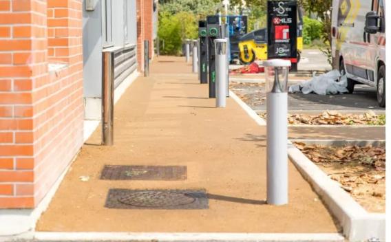 Trottoir en enrobé coloré posé dans un aménagement urbain, bordé de bornes et d'espaces végétalisés.
