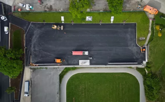 Vue aérienne d'un parking en cours d'enrobage : camions et engins disposés sur une surface fraîchement asphaltée, mise en perspective depuis un drone, illustrant phasage des travaux et organisation logistique.