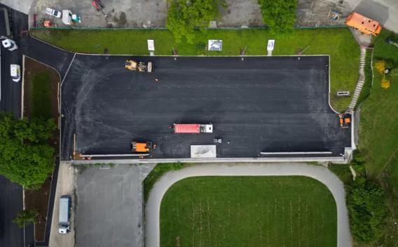 Vue aérienne d'un parking en cours d'enrobage : camions et engins disposés sur une surface fraîchement asphaltée, mise en perspective depuis un drone, illustrant phasage des travaux et organisation logistique.