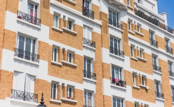 Bâtiment par Colas : Façade d’immeuble en brique et enduit blanc : alignement de baies vitrées avec garde-corps métalliques noirs, balcons ponctuels et modénatures géométriques typées art déco.