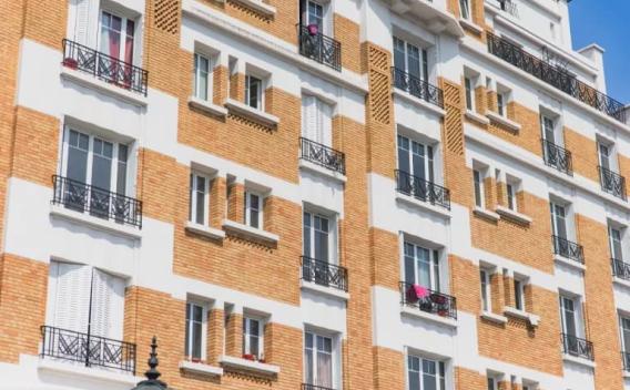 Bâtiment par Colas : Façade d’immeuble en brique et enduit blanc : alignement de baies vitrées avec garde-corps métalliques noirs, balcons ponctuels et modénatures géométriques typées art déco.