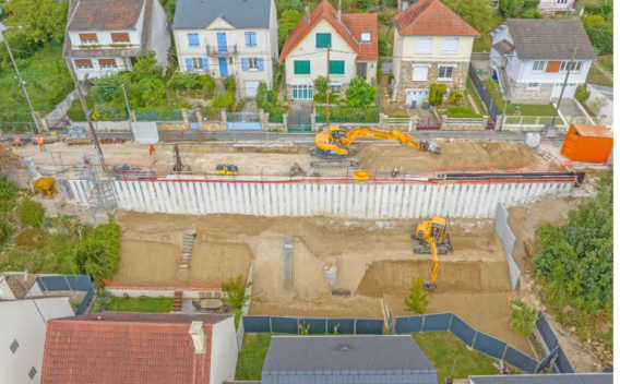 Génie civil par Colas : Vue aérienne d’un chantier de soutènement en zone résidentielle montrant palplanches installées, terrassement en cours et engins de chantier avec signalisation et stockage sur place.