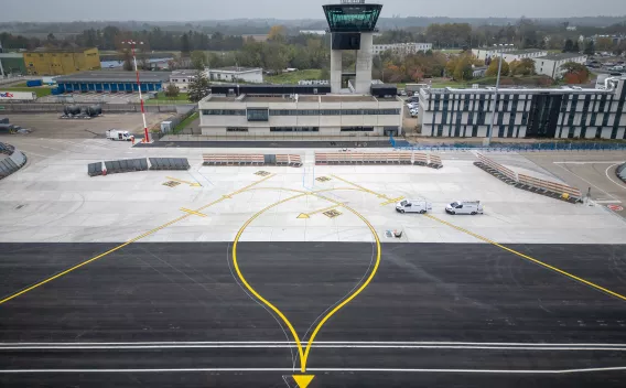 Aéroport de Strasbourg-Entzheimb : Aire de trafic d’aéroport fraîchement réaménagée avec marquages jaunes et blancs, vue vers la tour de contrôle et les bâtiments terminaux en arrière-plan.