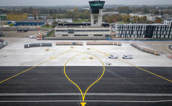 Aéroport de Strasbourg-Entzheimb : Aire de trafic d’aéroport fraîchement réaménagée avec marquages jaunes et blancs, vue vers la tour de contrôle et les bâtiments terminaux en arrière-plan.