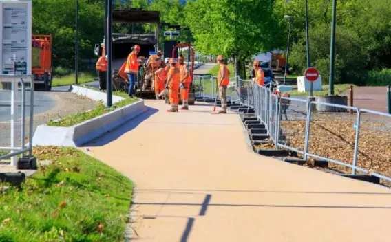 Équipe de chantier en haute visibilité réalisant la pose et la finition d’un revêtement piétonnier sur trottoir sécurisé, avec engins et balisage de sécurité.