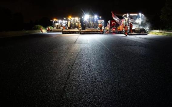 Chantier de pose d’enrobé de nuit avec une ligne d’engins éclairés et opérateurs en EPI assurant une intervention sécurisée pour la rénovation d’une chaussée.