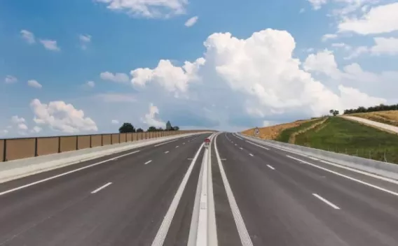 Chaussée neuve sur voie rapide : revêtement bitumineux posé, glissières et marquages centraux en place pour circulation à grande vitesse.