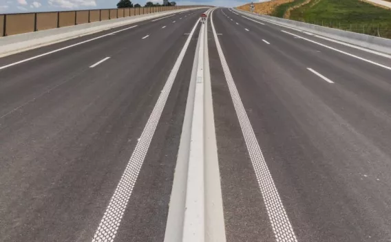 Autoroute neuve à plusieurs voies avec séparateur central en béton et bandes rugueuses de guidage, surface en enrobé lisse prête à la circulation.