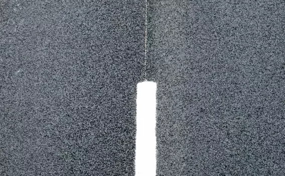 Gros plan d’un marquage routier blanc sur une surface d’enrobé granuleuse, mettant en valeur la texture du revêtement et le contraste entre la bande verticale et l’asphalte sombre.