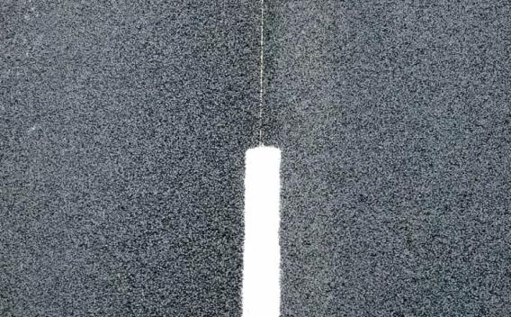 Gros plan d’un marquage routier blanc sur une surface d’enrobé granuleuse, mettant en valeur la texture du revêtement et le contraste entre la bande verticale et l’asphalte sombre.