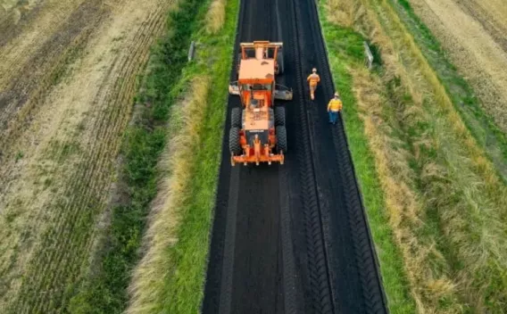 Raboteuse sur voie rurale encadrée de champs, deux opérateurs à pied supervisant une passe de fraisage.