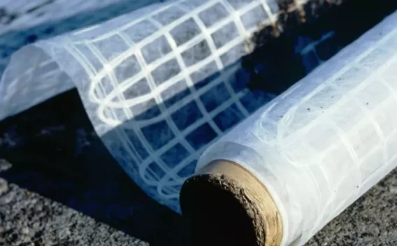 Rouleau de géogrille prêt à être déployé sur chaussée pour renforcer la structure avant la pose des enrobés.
