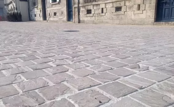 Surface pavée en dalles et pavés clairs formant une voie piétonne urbaine entre façades anciennes.