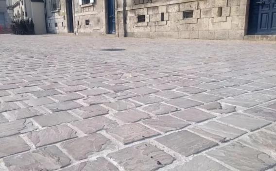 Surface pavée en dalles et pavés clairs formant une voie piétonne urbaine entre façades anciennes.