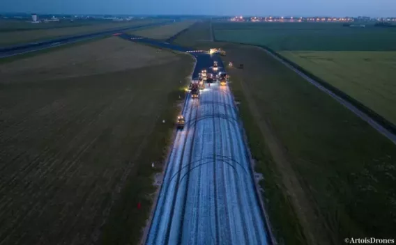 Chantier nocturne d'enrobage/renouvellement routier vu en drone, montrant une file de machines opérant sur une chaussée fraîchement traitée.