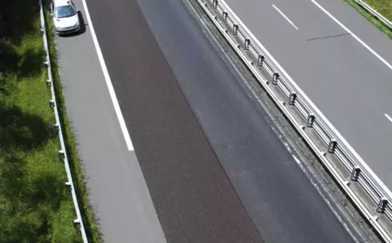 Vue aérienne d’une chaussée en réparation : une raboteuse et une couche d’enrobé fraîchement posée longent l’autoroute, avec balisage de chantier et circulation réduite.