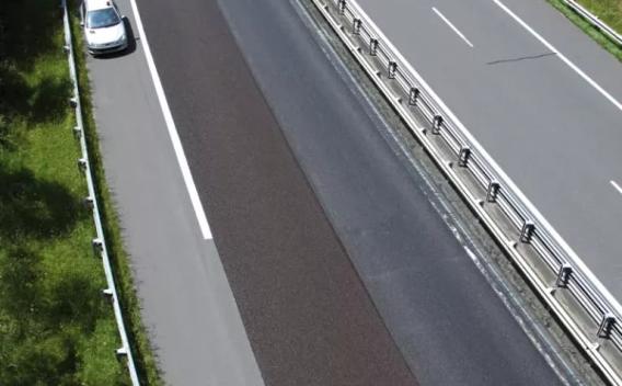 Vue aérienne d’une chaussée en réparation : une raboteuse et une couche d’enrobé fraîchement posée longent l’autoroute, avec balisage de chantier et circulation réduite.