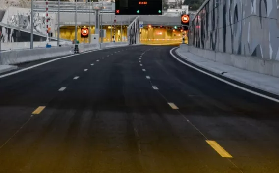 Chaussée neuve menant à une galerie urbaine, surface d’enrobé fraîche avec marquages provisoires et dispositifs de signalisation.